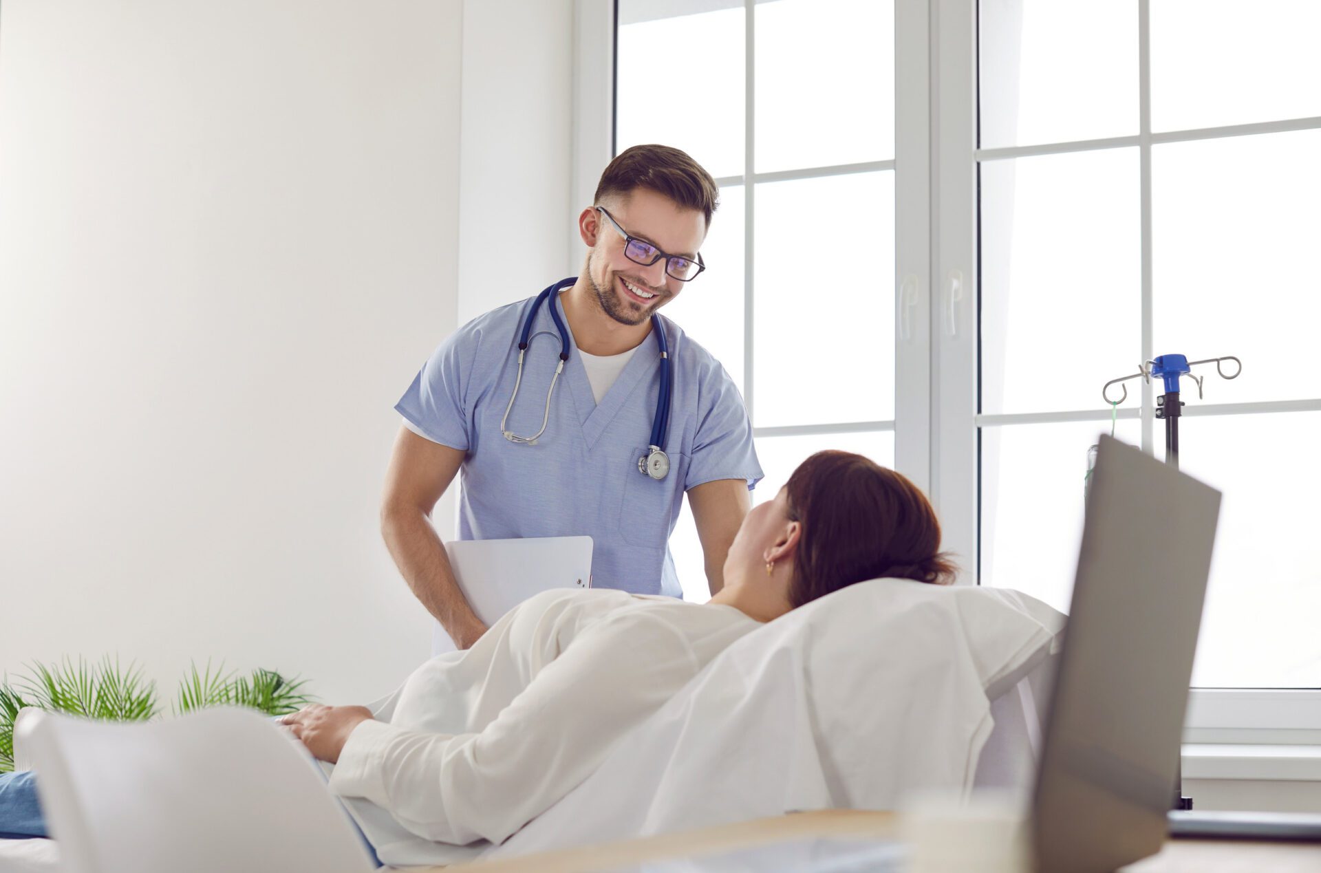 Friendly male nurse gives IV line to woman patient who is lying on medical bed at clinic